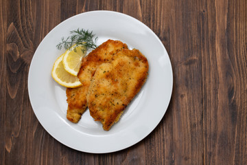 fried chicken with lemon on white plate on brown wooden background