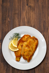 fried chicken with lemon on white plate on brown wooden background