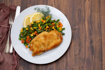fried chicken with boiled vegetables and lemon on white dish