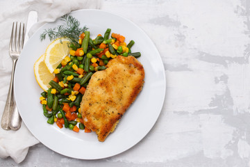 fried chicken with boiled vegetables and lemon on white dish