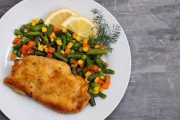 fried chicken with boiled vegetables and lemon on white dish