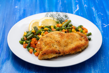 fried chicken with boiled vegetables and lemon on white dish