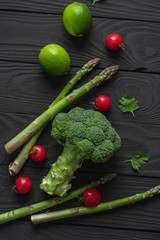 Asparagus pods, lime, green broccoli and red cherry tomatoes on a black wooden table