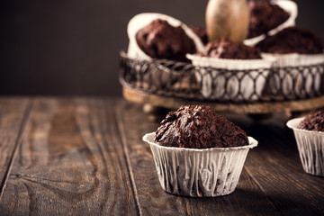 Chocolate muffins with banana in white paper cups on dark wooden background. Party food concept with copy space.