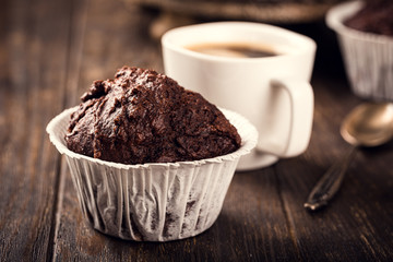 Chocolate muffins with banana in white paper cups on dark wooden background. Party food concept.