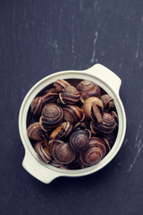 boiled snails with herbs in white dish on ceramic background