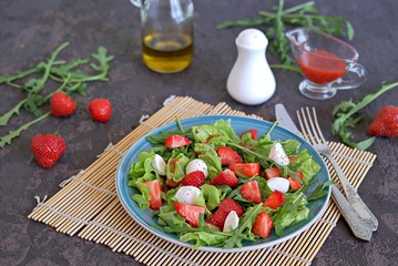Salad with strawberries, arugula and mozzarella cheese on a dark brown background concrete. Healthy food.