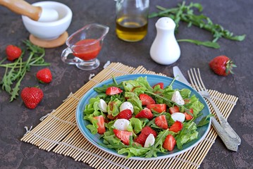 Salad with strawberries, arugula and mozzarella cheese on a dark brown background concrete. Healthy food.
