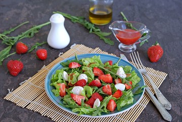 Salad with strawberries, arugula and mozzarella cheese on a dark brown background concrete. Healthy food.