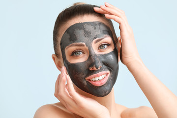 Beautiful young woman with facial mask on color background