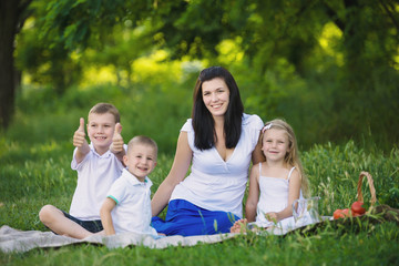 Happy woman with her three kids sits on the plaid outdoor. Family picnic