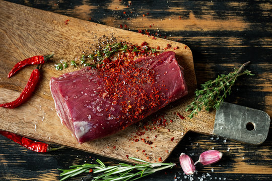 Beef fillet steak cooking with herbs, spices, garlic, salt and pepper on wooden table background.