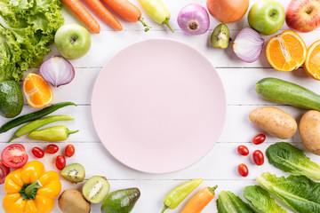 Healthy lifestyle and food concept. Top view of fresh vegetables, fruit, herbs and spices with a empty pink pastel plate on white wooden background.