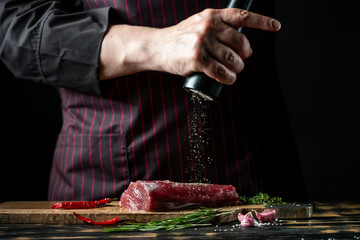 Butcher chef cooking meat fillet and adding salt, pepper and chili for marinade on black background.
