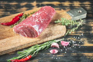 Beef fillet steak cooking with herbs, spices, garlic, salt and pepper on wooden table background.