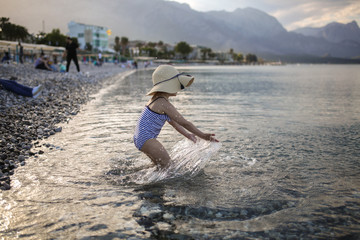 child in striped swimsuit and hat splashing in sea