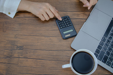 The index finger pointing to the calculator key.Computer calculators and white coffee cups placed on a brown desk.Do not focus on objects.