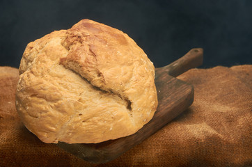 Fresh homemade bread on a wooden board against a dark background.