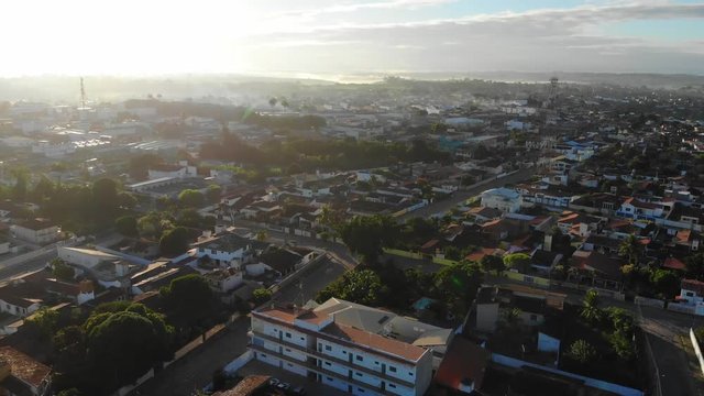 Sunset Aerial shot of a low-income urban area in Cruz das Almas, Bahia, Brazil. Show houses, small buildings in the neighborhood, and green environnement. Drone slowly moving up.