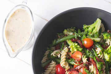 Cold Italian salad with pasta and vegetables in black bowl on white background.