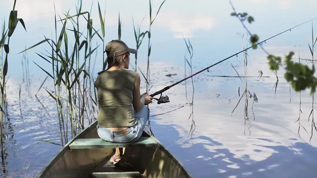 Young woman fisherman is fishing on the forest lake, holding the fishing rod twists the coil.