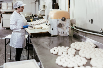 Young female worker working in large bakery. Bread preparation.