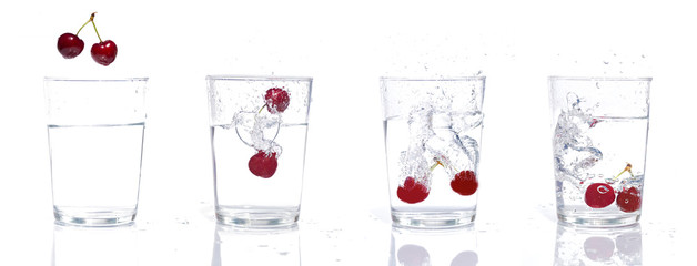 High-speed stream of two cherries falling into a glass with water. Isolated image that gives a sensation of freshness