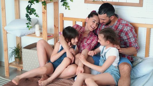 Happy parents and two daughters have good time together at home, sit on bed