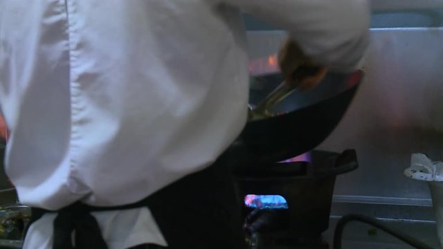 Close-up low-angle still shot of a chef wearing a white gown and black apron preparing a light vegetable meal at a restaurant kitchen, Lima Peru