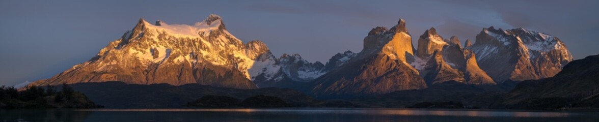 Panorama of Torres del Paine National Park with snow capped mountains (Cordillera Paine) and calm lake of Pehoe at sunrise. Chile