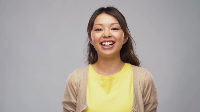 portrait, emotions and people concept - smiling young asian woman in cardigan over grey background