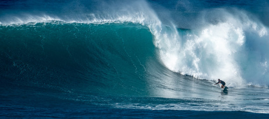 Surfer rides giant wave at the famous Waimea Bay surf spot located on the North Shore of Oahu in...