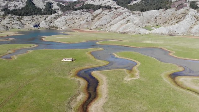 top view of a plateau of the Italian Apennines with lake and mountains in the background. green fields and mountains with a lake and a cottage, pristine nature and summer season. Aerial footage