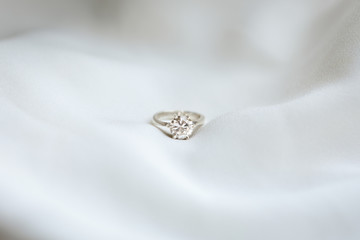A wedding ring lies on a white wedding dress