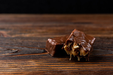 Chocolate sweet with caramel and peanut on dark wooden background.