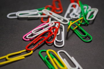 On black monophonic background plastic multi-colored paper clips   are lie. White, red, green, yellow colors. Office.