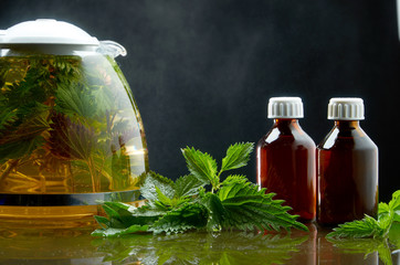 Tea teapot of fresh nettle and nettle leaves in a medical environment on a black background