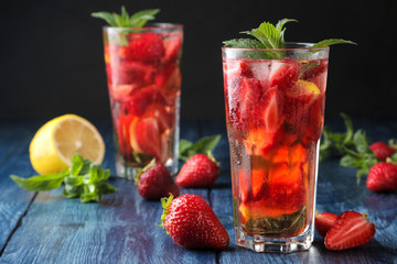 Strawberry Mojito. Cold summer mojito cocktail with strawberries, mint, lemon and ice in a glass on a blue wooden table. on a dark background