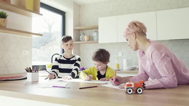 A young mother with two children drawing in a kitchen.