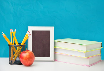 Stack of books with apple, and pencils near empty green chalkboard. Sample for text.