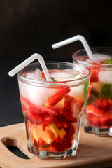 Strawberry Mojito. Cold summer mojito cocktail with strawberries, mint, lemon and ice in a glass on a black table. on a dark background