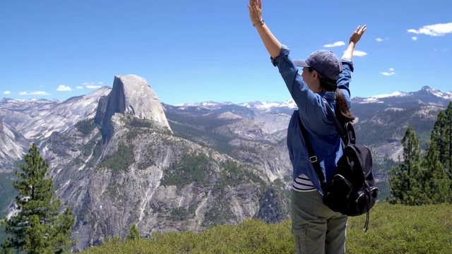 back view of happy woman hiker with backpack enjoying nature on grass meadow on top of mountain cliff with sunshine outdoor. Freedom concept. half dome trail view yosemite national park california