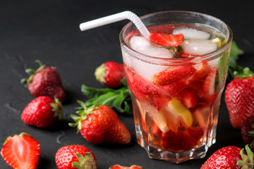 Strawberry Mojito. Cold summer mojito cocktail with strawberries, mint, lemon and ice in a glass on a black table. on a dark background
