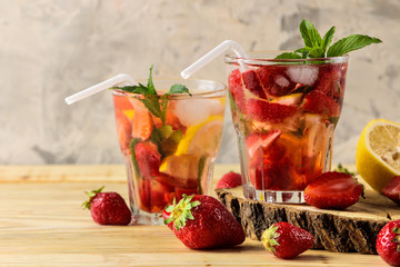 Strawberry Mojito. Cold summer mojito cocktail with strawberries, mint, lemon and ice in a glass on a natural wooden table. summer refreshing drink.
