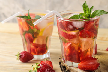 Strawberry Mojito. Cold summer mojito cocktail with strawberries, mint, lemon and ice in a glass on a natural wooden table. summer refreshing drink.