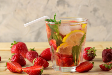 Strawberry Mojito. Cold summer mojito cocktail with strawberries, mint, lemon and ice in a glass on a natural wooden table. summer refreshing drink.