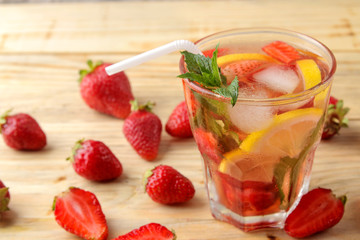 Strawberry Mojito. Cold summer mojito cocktail with strawberries, mint, lemon and ice in a glass on a natural wooden table. summer refreshing drink.