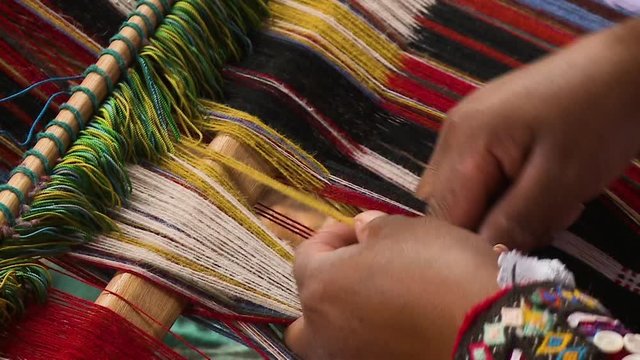Extreme close-up high-angle still shot of a country side woman carefully creating weaving patterns on a small handloom, Andes, Peru