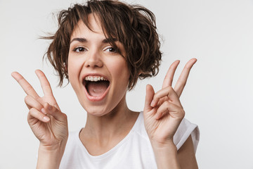 Excited happy woman posing isolated over white wall background showing peace gesture.
