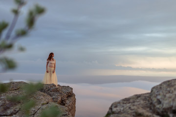 A girl in a dress and hat admiring the dawn or sunset of the sun in a picturesque place in the mountains.
